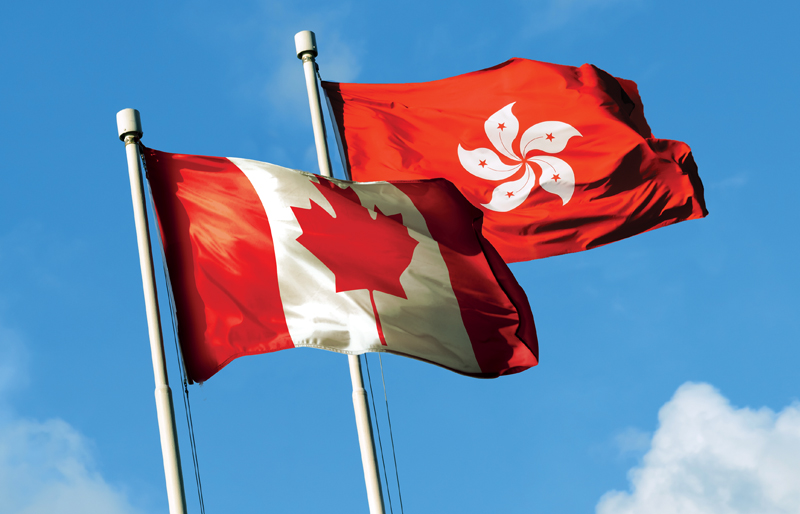 Photo of both the Hong Kong flag and Canadian flag  blowing in the breeze side-by-side