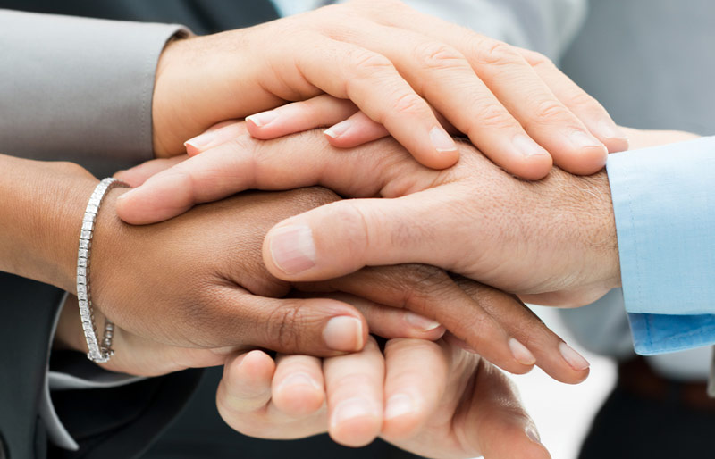 Close-up of businesspeople placing their hands together, one over the other in a form of team huddle.