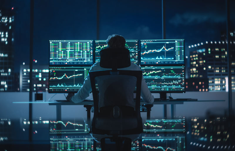 Un homme d'affaires examine des écrans d'ordinateur avec des données financières, un paysage urbain en arrière-plan.
