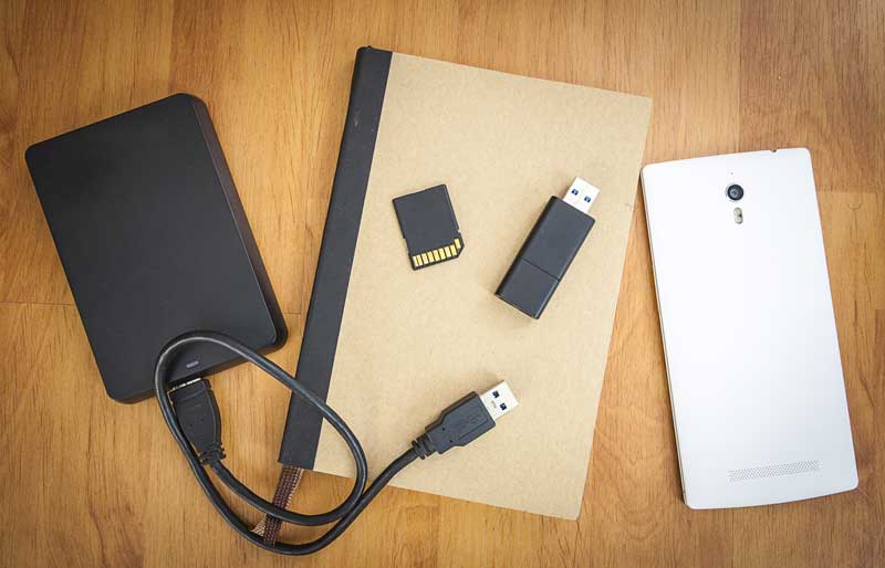Un disque dur externe, une clef USB, une carte SD, un carnet de notes et un cellulaire sont posés sur une table de bois
