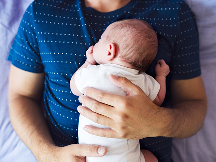 Un père tient un nouveau-né dans ses bras, se demandant : un bébé, combien ça coûte vraiment?