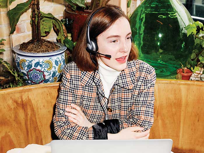 woman talking on a phone headset, in front of a laptop in a cafe
