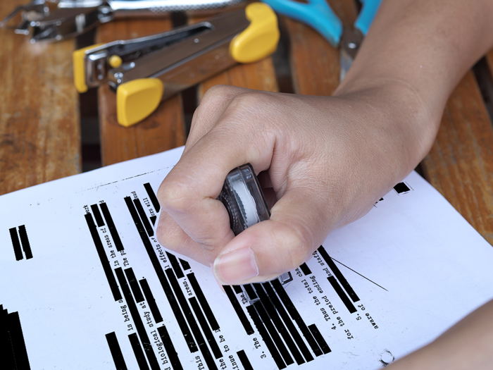 woman using a blackout roller to black out text on paper