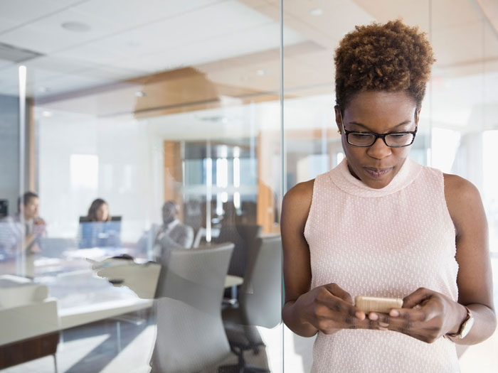 Businesswoman texting with cell phone outside conference room meeting