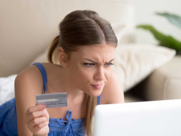 Une jeune femme confuse ayant un problème avec la carte de crédit bloquée a rejeté le paiement en ligne non sécurisé en utilisant un ordinateur portable à la maison, un compte périmé invalide, une transaction échouée, un retrait d'argent impossible, une dette