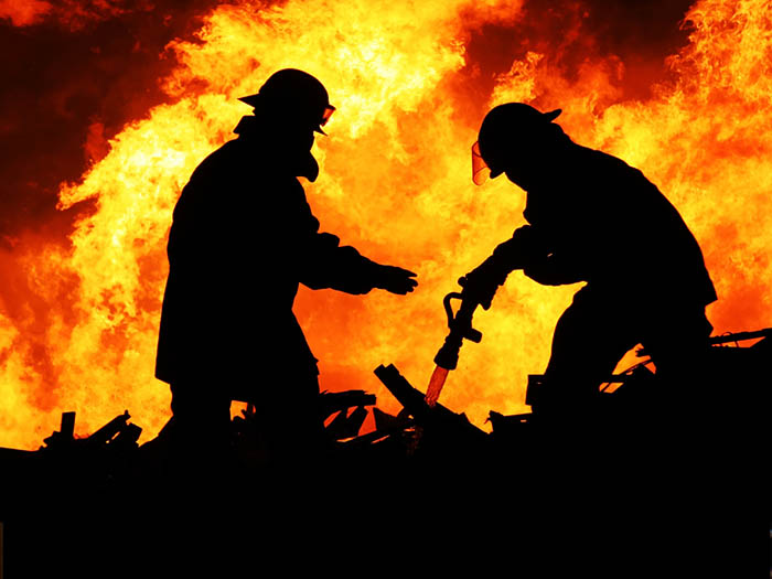 Silhouette of two firemen fighting a huge fire behind them