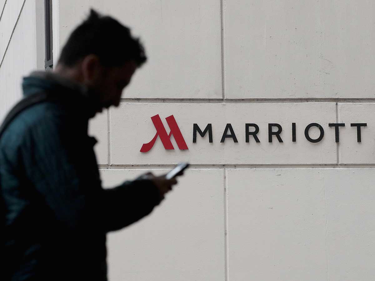 Silhouette of person on phone, in foreground, walking in front of Marriott hotel sign
