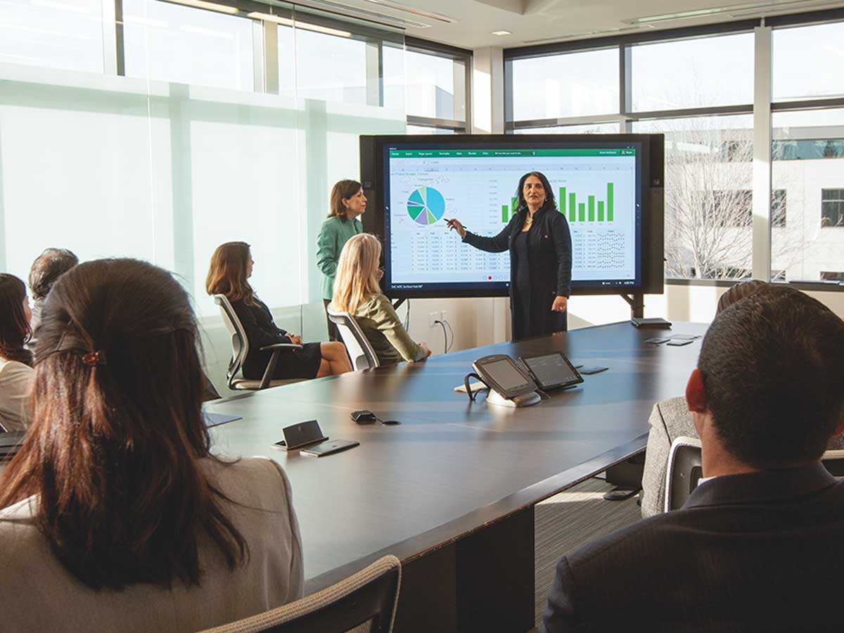woman presenting in front of a screen in a boardroom