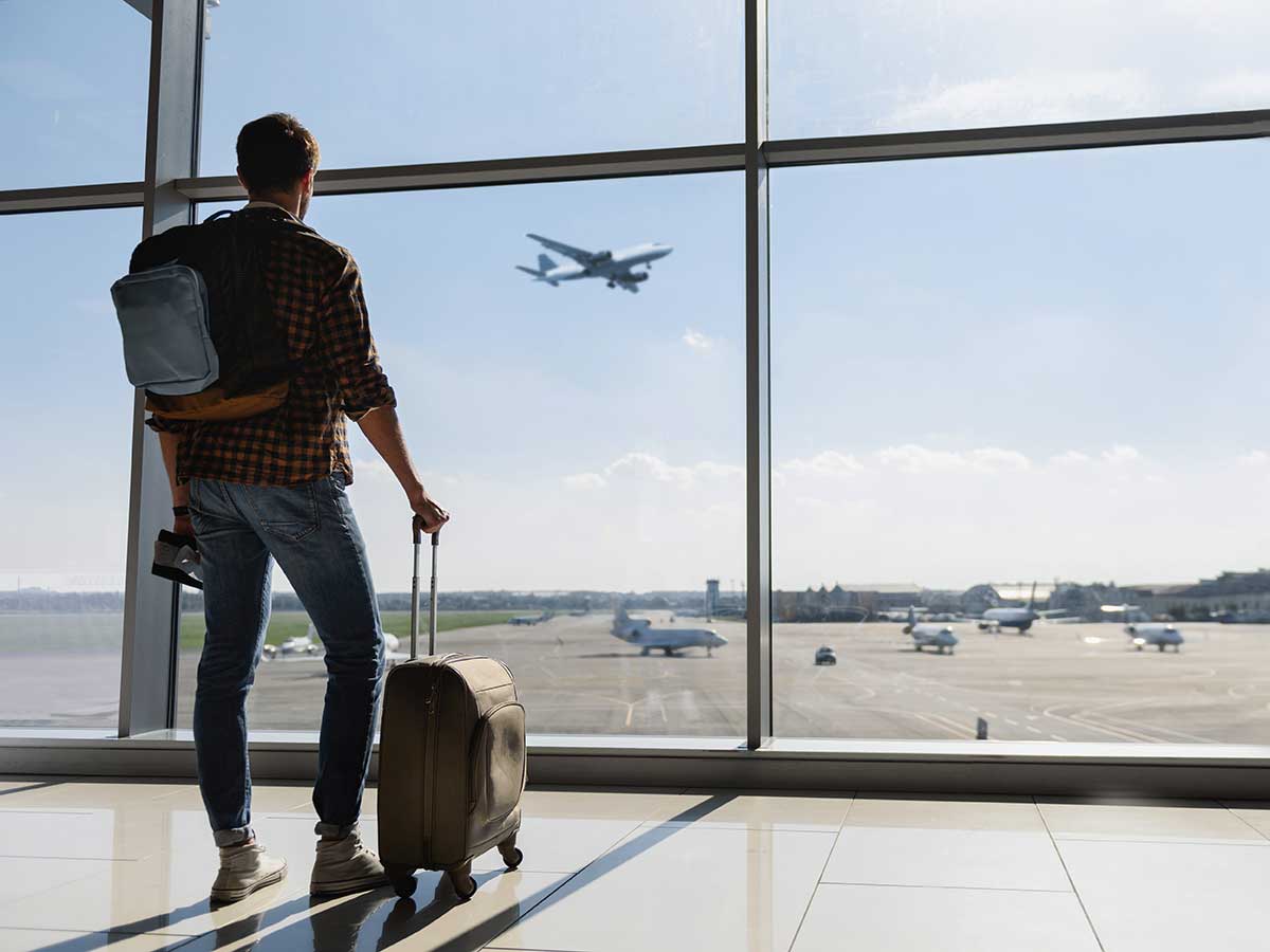 Jeune homme àvec bagage debout à fenêtre de l'aéroport et regarder l'avion avant départ