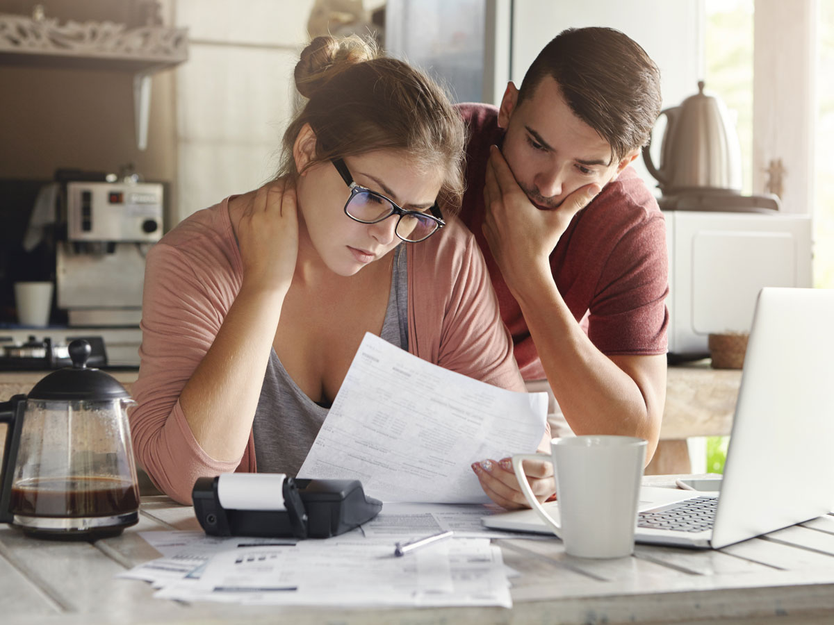 Young family having debt problems, not able to pay out their loan. Couple studying paper form bank while managing domestic budget together in kitchen