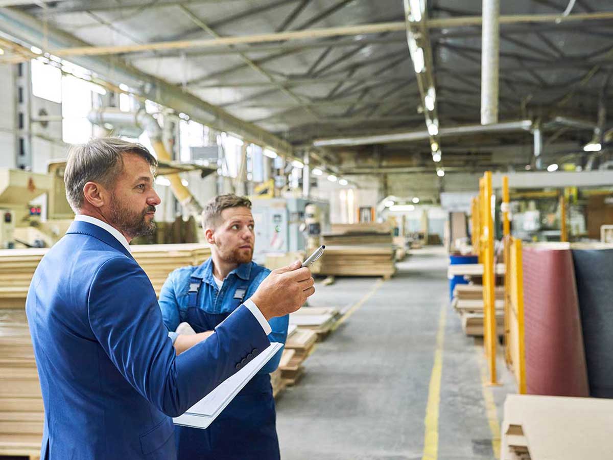 Mature businessman inspecting factory warehouse with younger workman