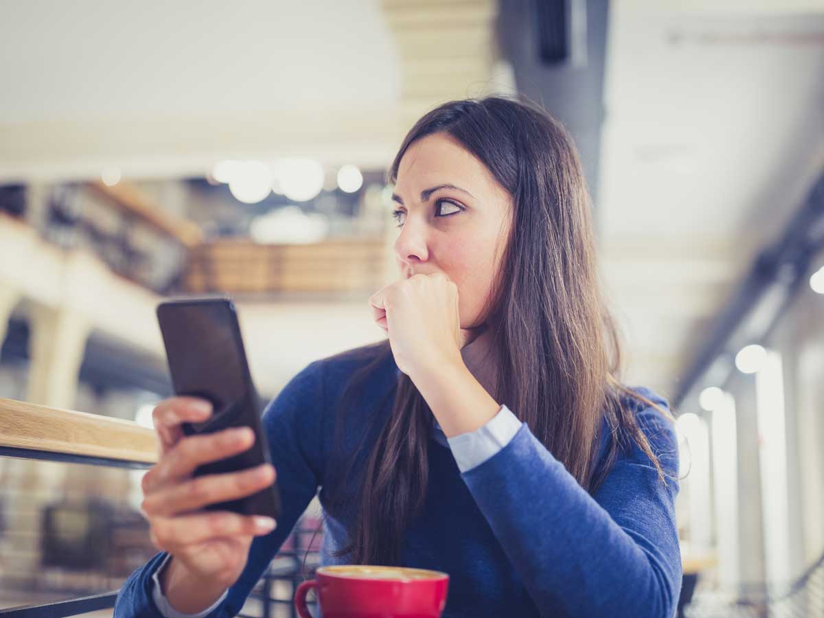 Worried young woman using smart phone in cafe