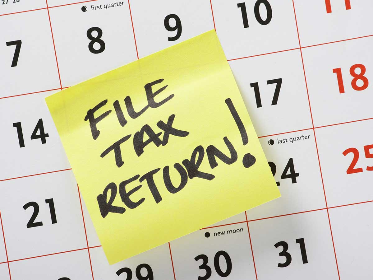 Hand written post-it note reminder to File Tax Return stuck to a calendar