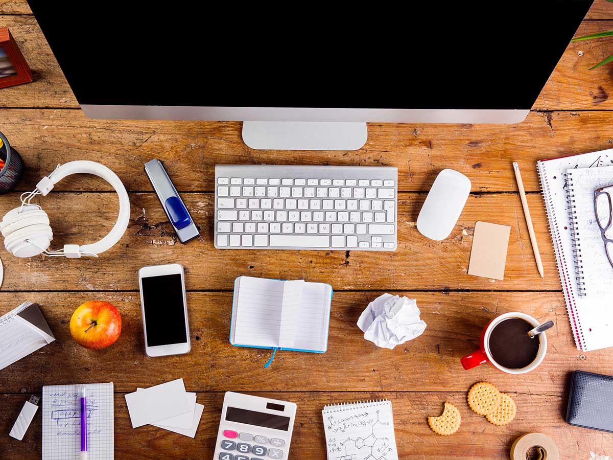 vue en hauteur d'un bureau en bois avec divers gadgets et fournitures de bureau disposés devant un clavier et un moniteur