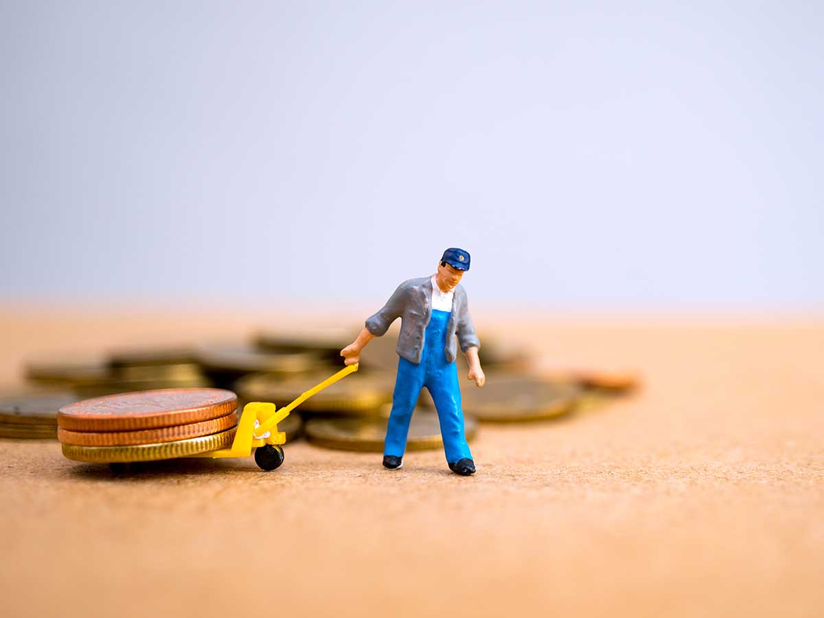 miniature figurine of trade worker pulling real coins on a miniature dolly