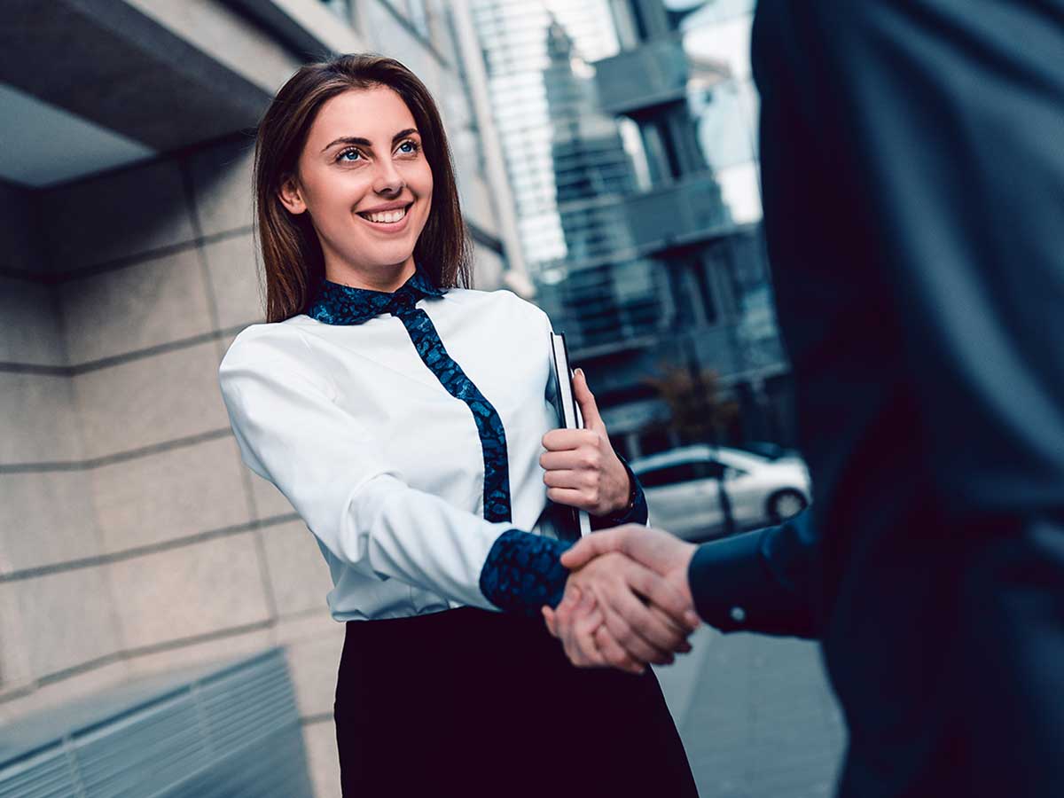 young business lady shaking hands with another business person outside a city building