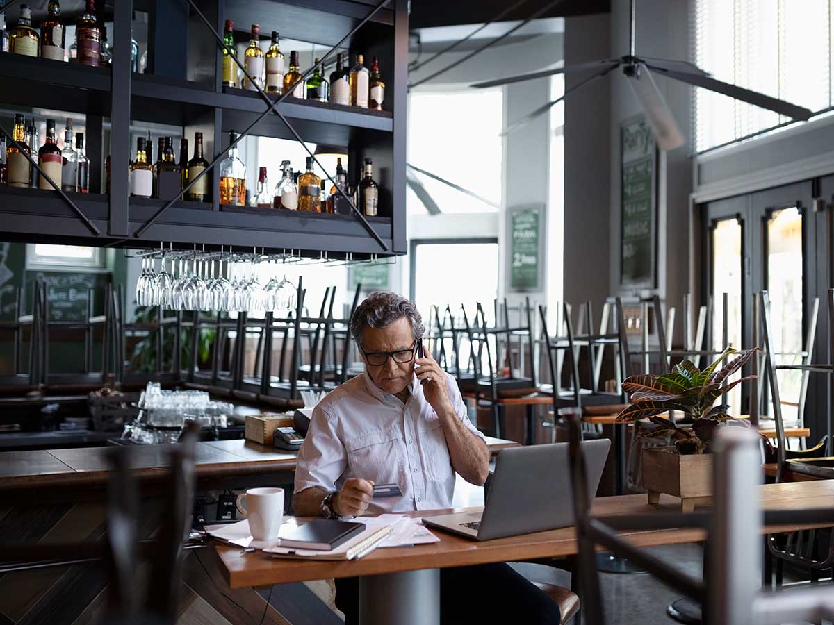Restaurant owner doing paperwork at laptop at table after hours