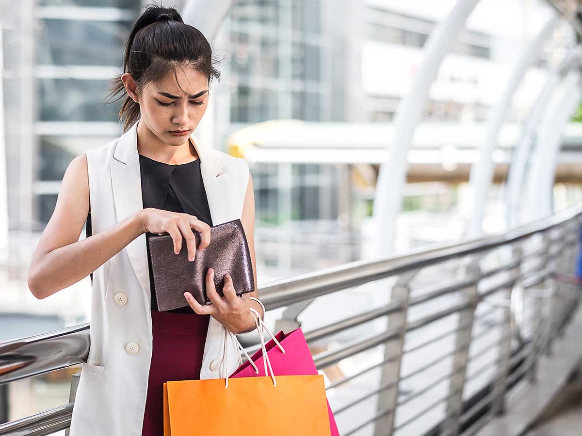 Young lady with shopping bags on her arm, looking worried that her wallet is empty
