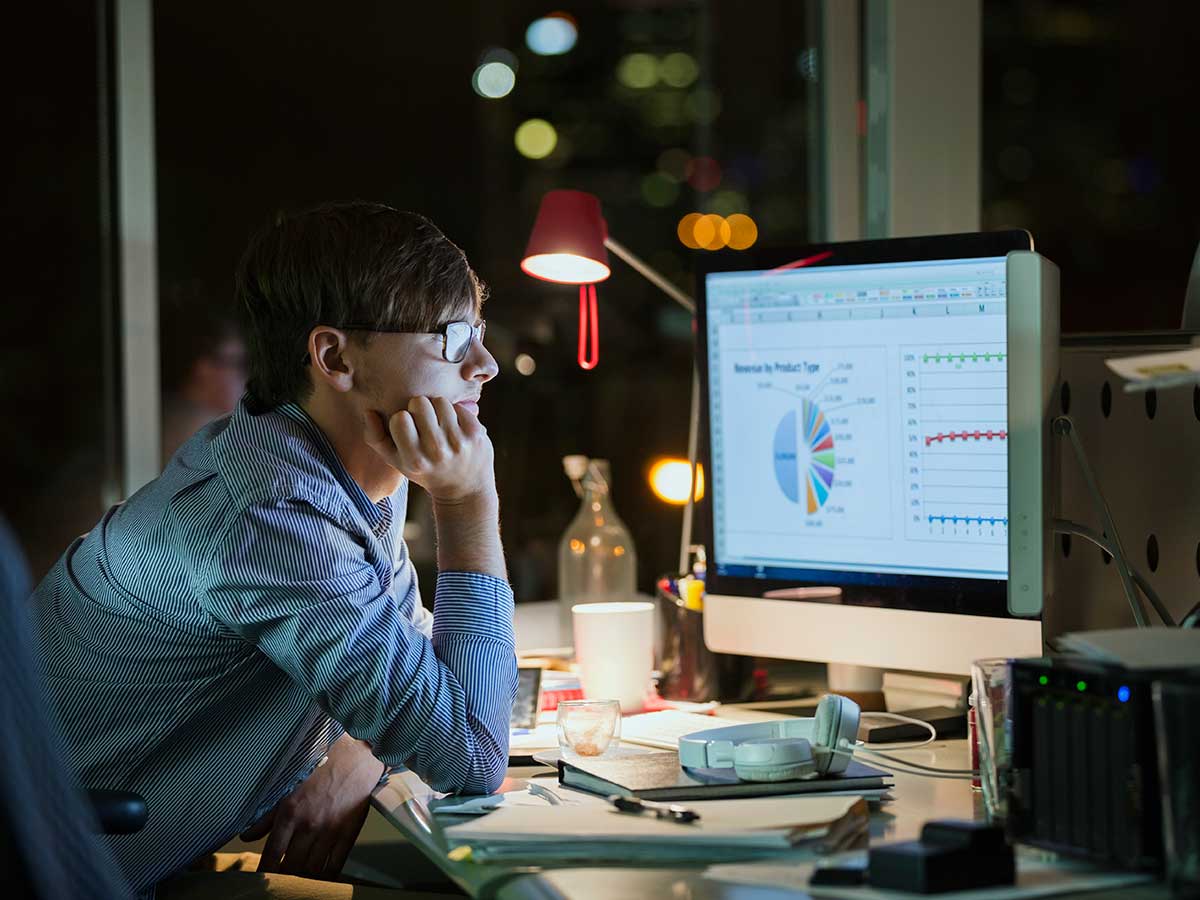 Office worker working late at night exmining business information on computer screen