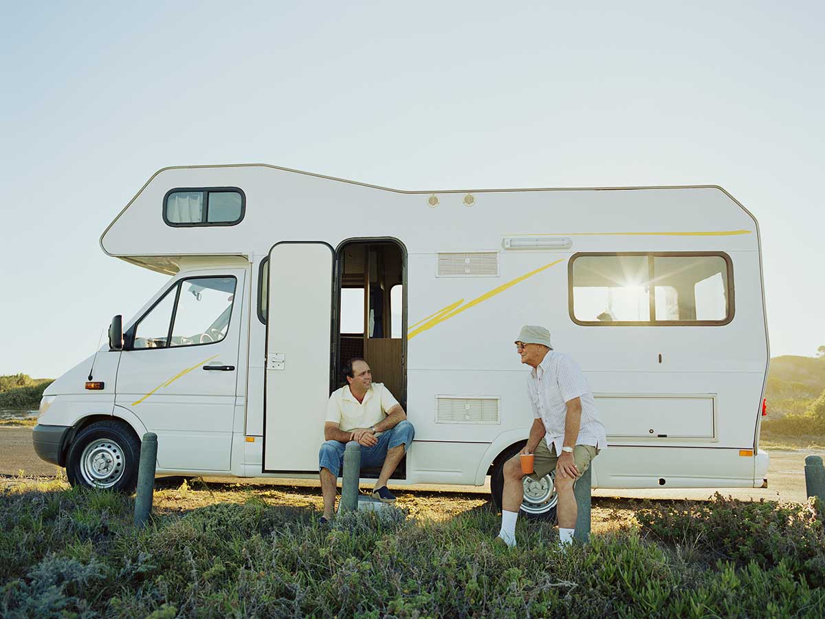 Two senior men relaxing outside their campervan with sun behind them