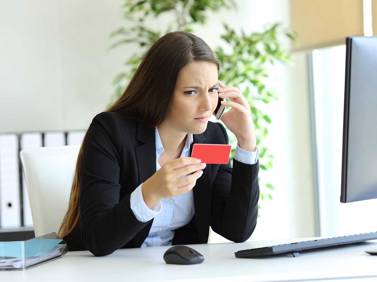 Femmes d'affaires confus sur un téléphone intelligent dans son bureau, tenant sa carte de crédit