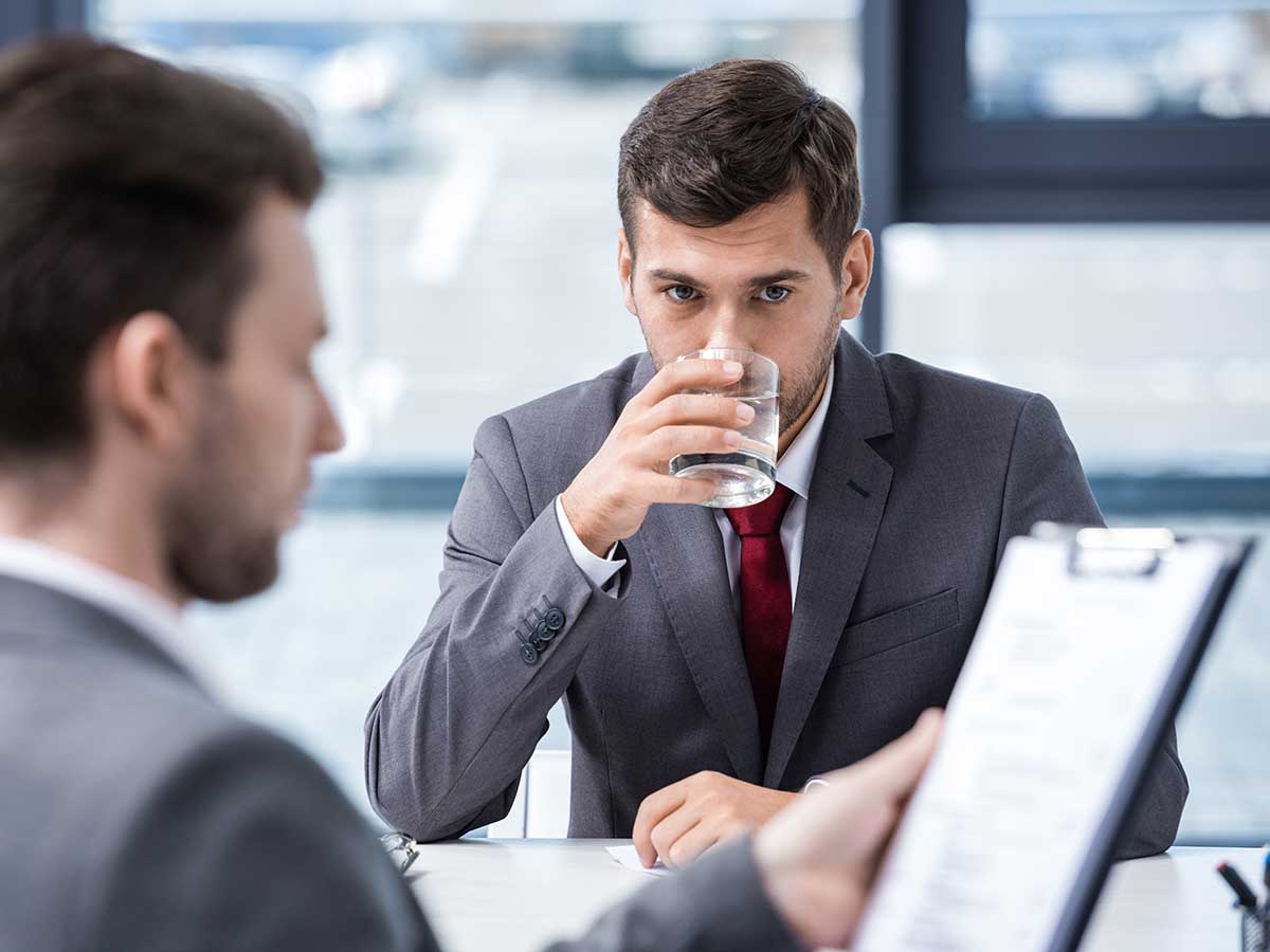 Jeune homme nerveux qui boit de l'eau dans un verre lors d'un entretien d'embauche
