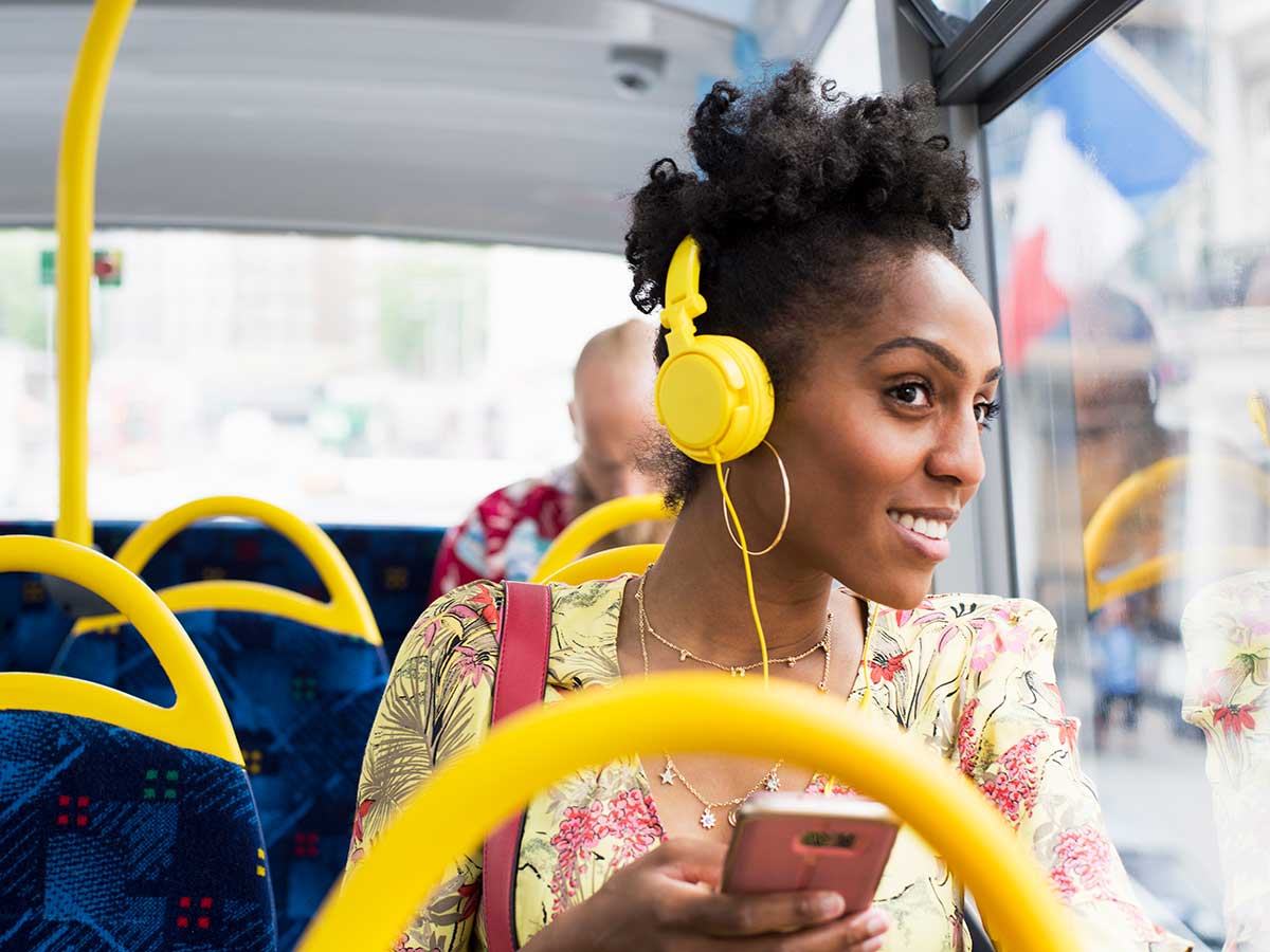 Happy young lady relaxing on a bus wearing headphones, listening to music