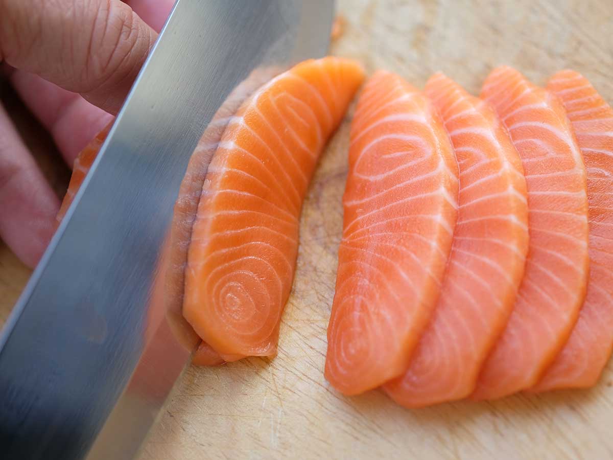 cutting fresh salmon fillet on chopping board 