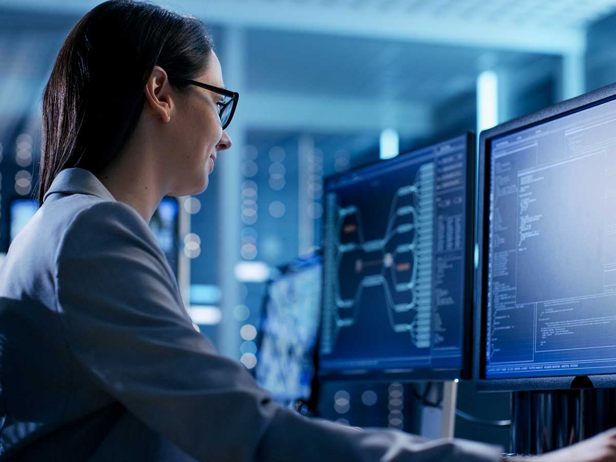 Femme devant un ordinateur dans une pièce remplie de serveurs, vérifiant les données à l'écran
