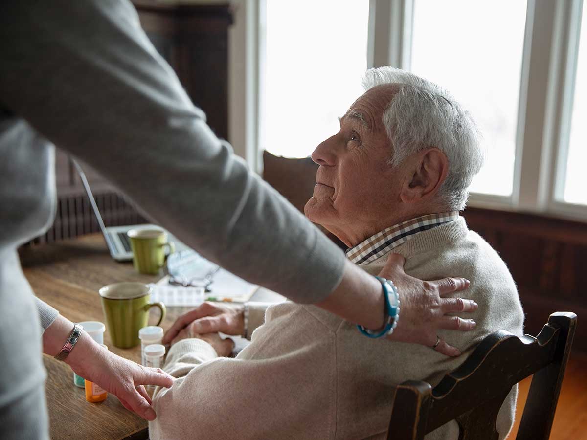 soignant réconfortant homme senior à table dans sa maison