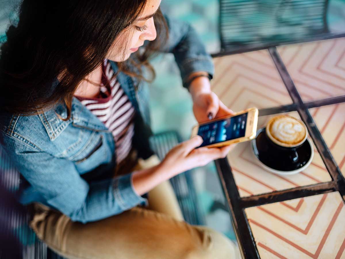 Jeune femme à l'aide d'un appareil intelligent pour vérifier les finances dans un café