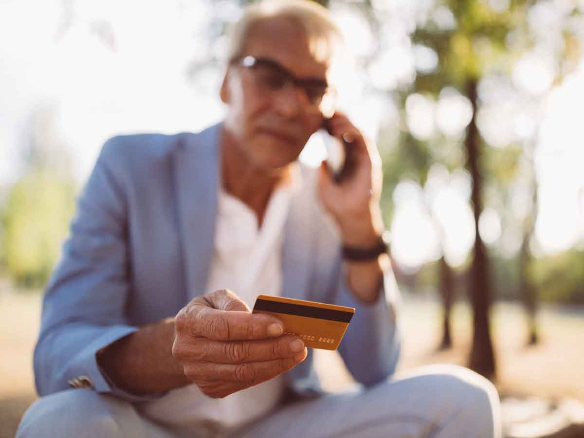 Senior homme au téléphone avec carte de crédit en main
