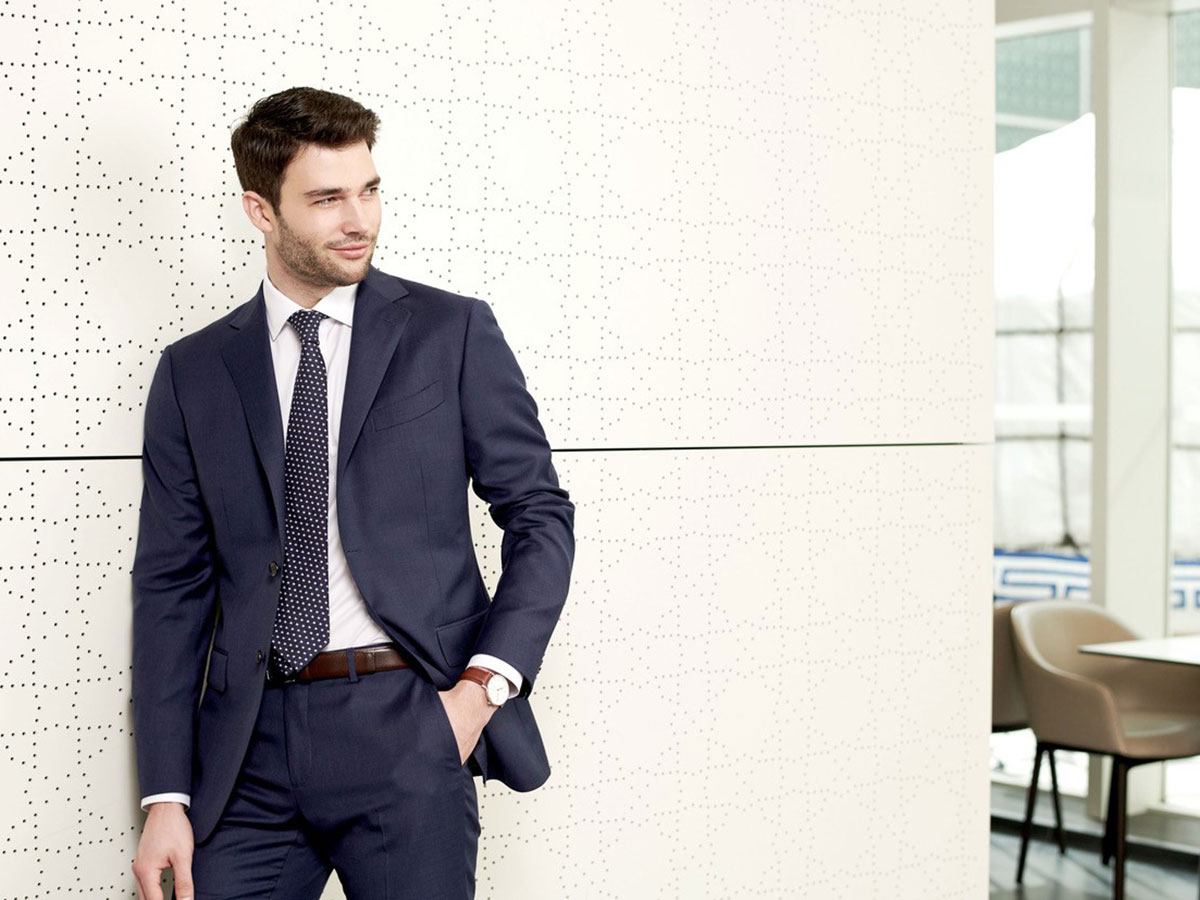 male model wearing dark blue business suit while standing by wall