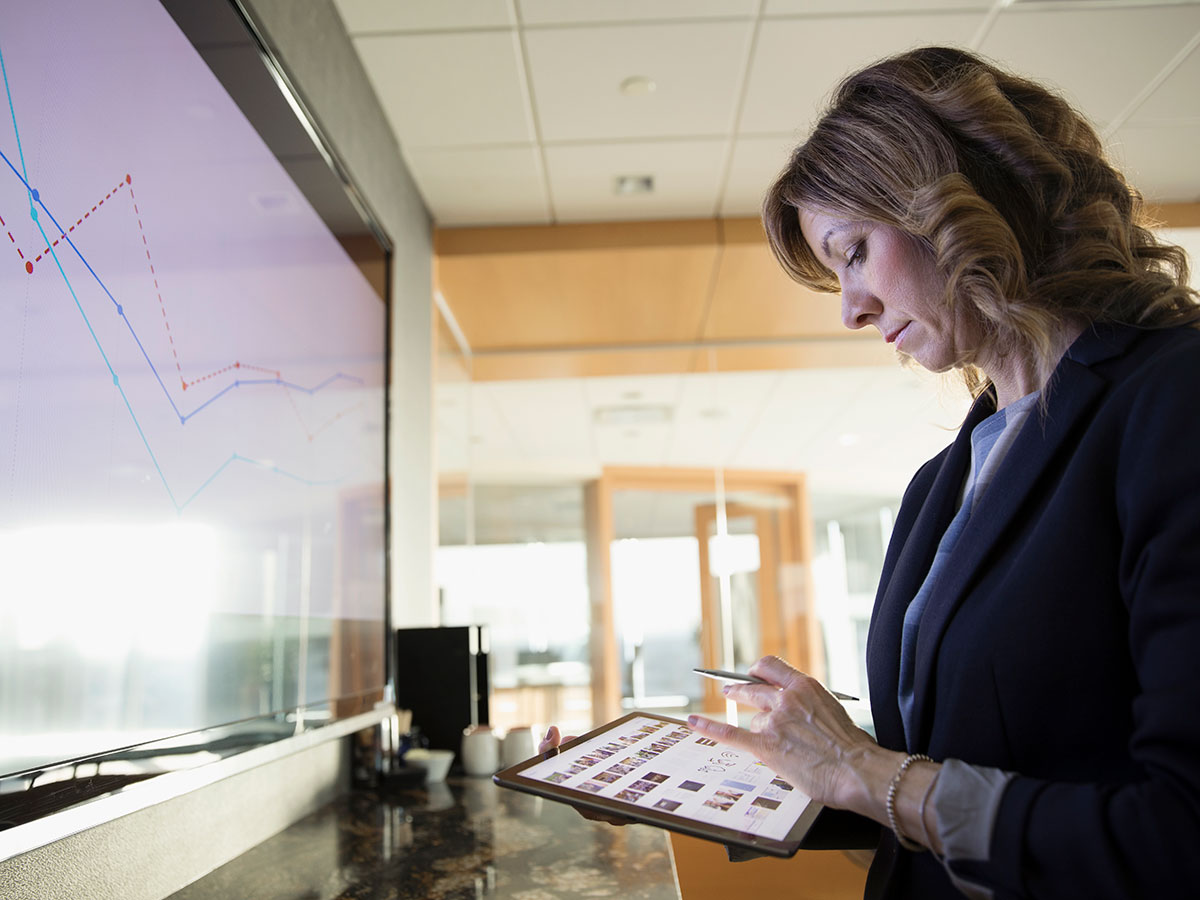 femme d'affaires à l'aide d'une tablette face à un écran de présentation en salle de réunion