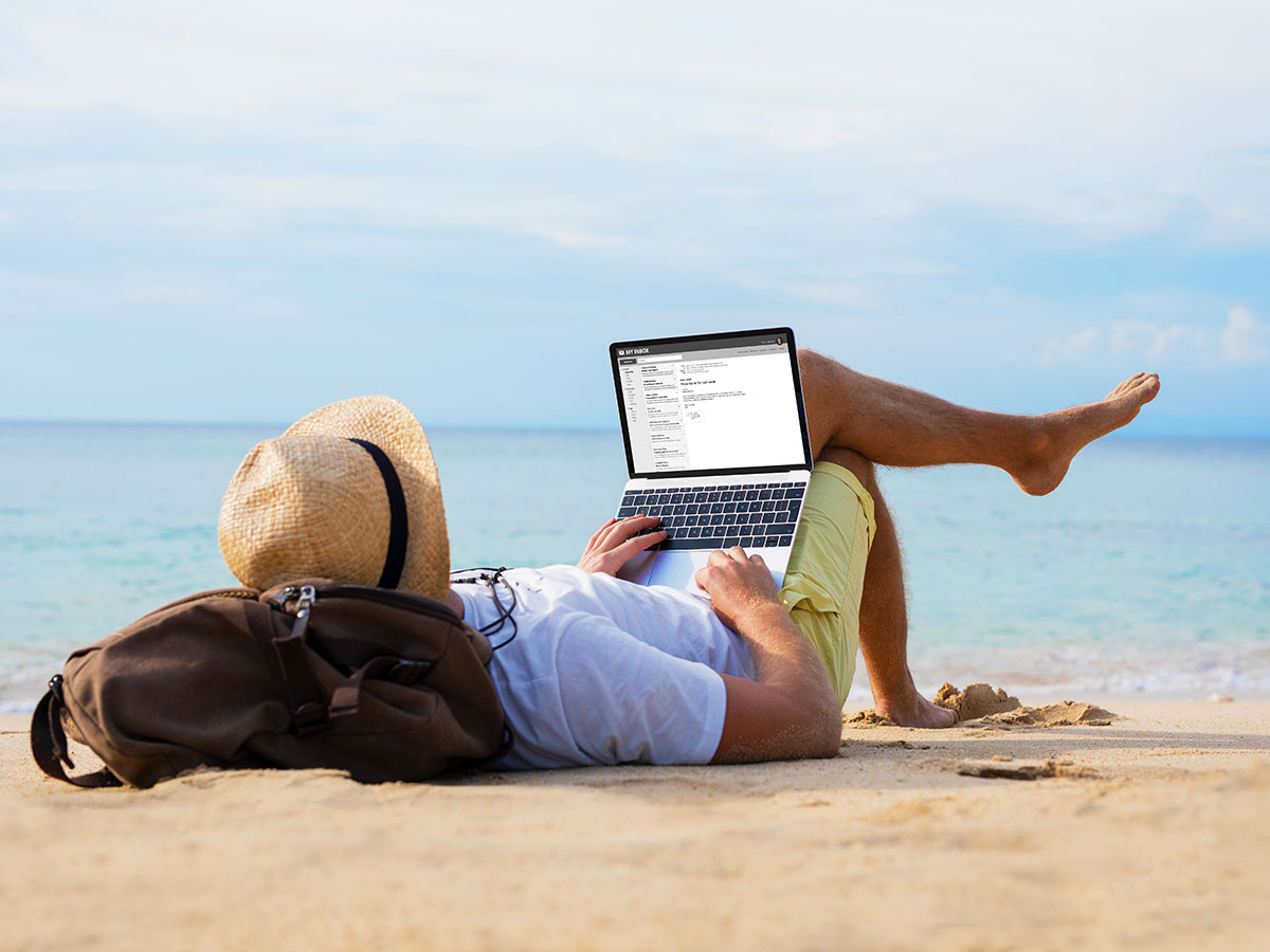 young man relaxing on beach, while reading emails on laptop