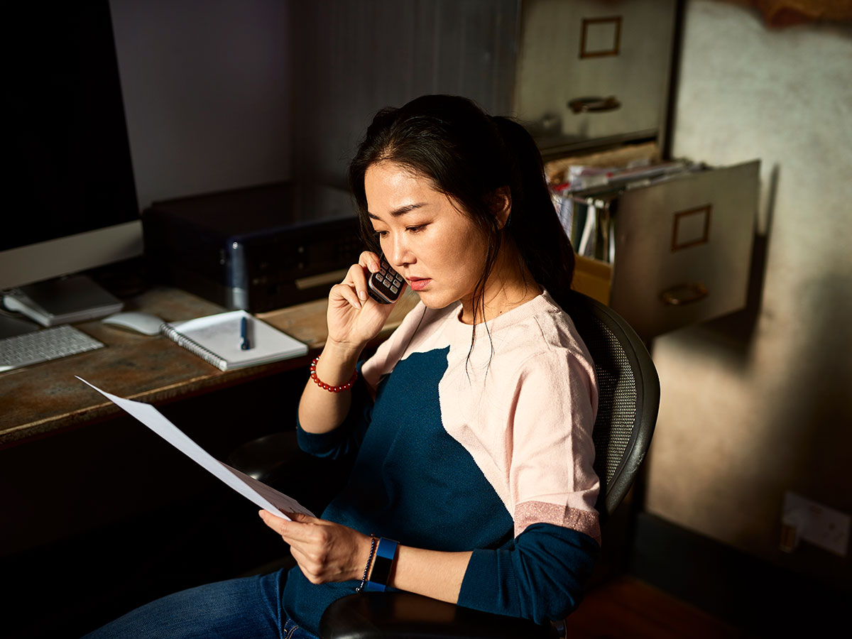 young woman on a cell phone in her home office, while looking at a important document