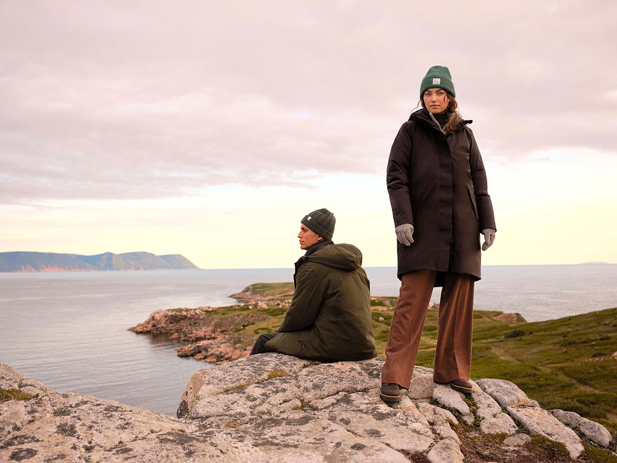 Male and female model on rocky shoreline, wearing winter jackets
