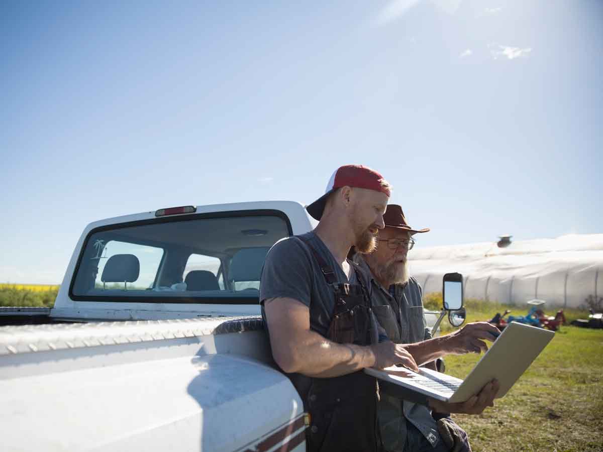 Père et fils d'agriculteurs à l'aide d'un ordinateur portable à la camionnette sur une journée ensoleillée à la ferme
