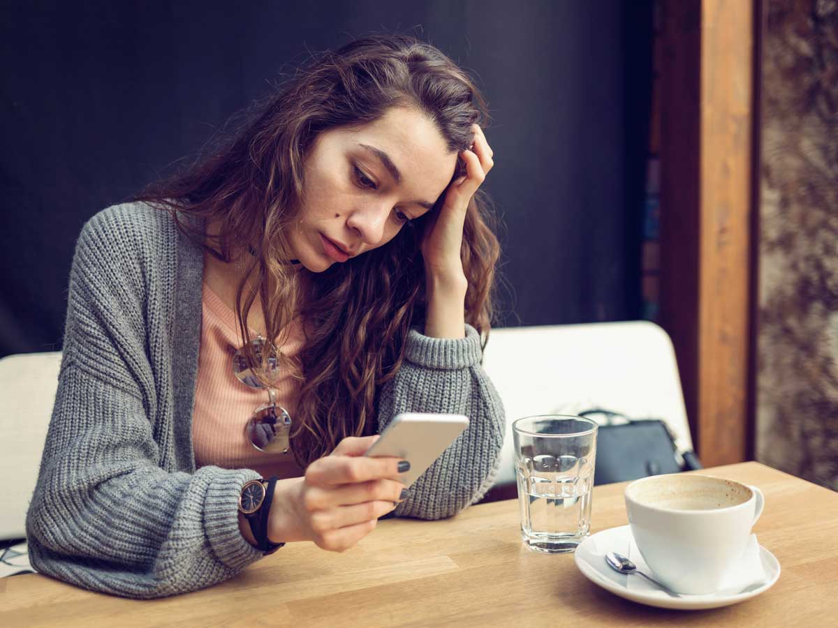 Woman sitting in cafe, looking at her phone with concern