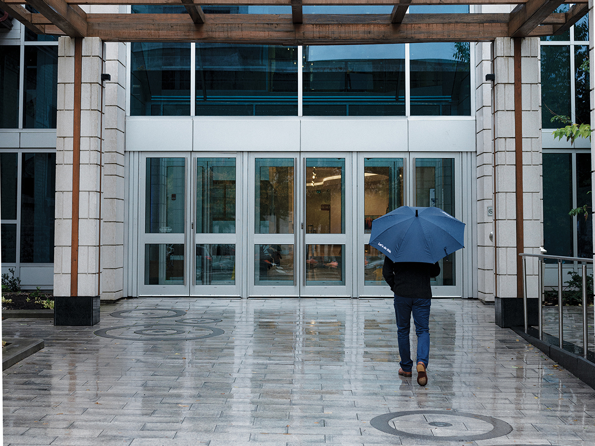 Person holding umbrella walks toward office building