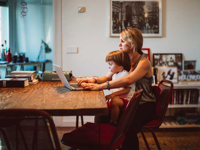 Une jeune femme travaille à domicile avec un enfant assis sur ses genoux