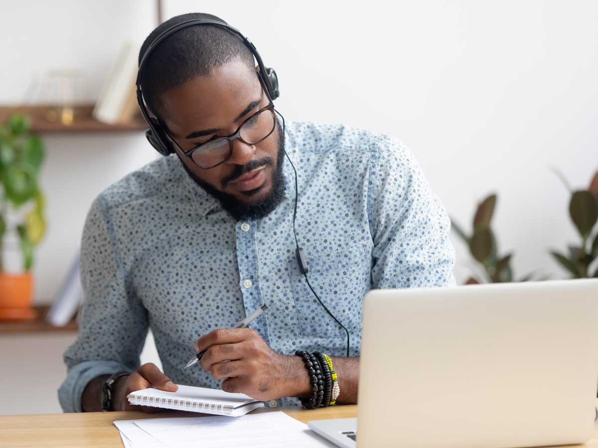 Focused businessman in headphones writing notes watching webinar