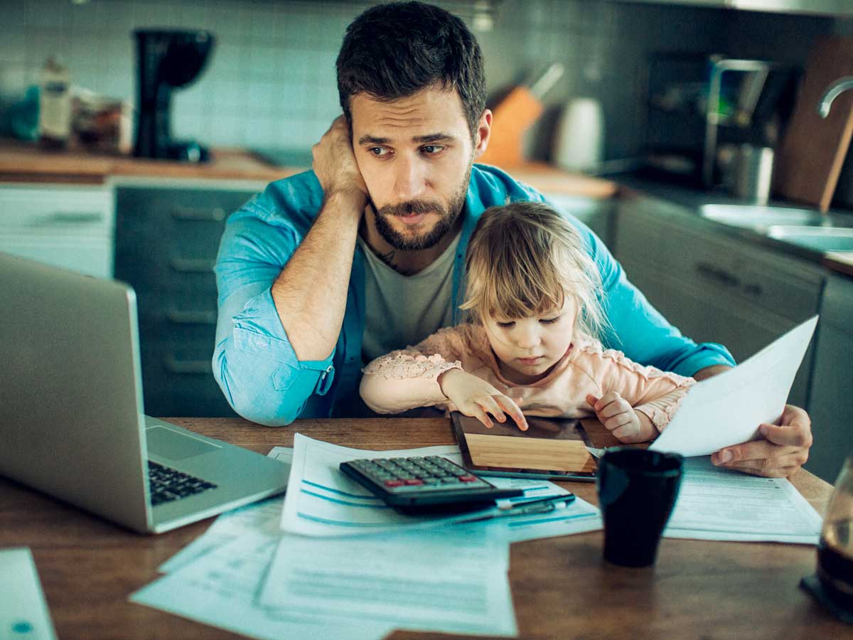 Father sitting at kitchen table with toddler on lap looking over bills