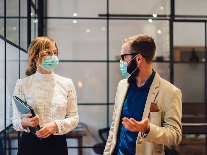 Homme et femme parlant dans le couloir du bureau tout en portant des masques chirurgicaux