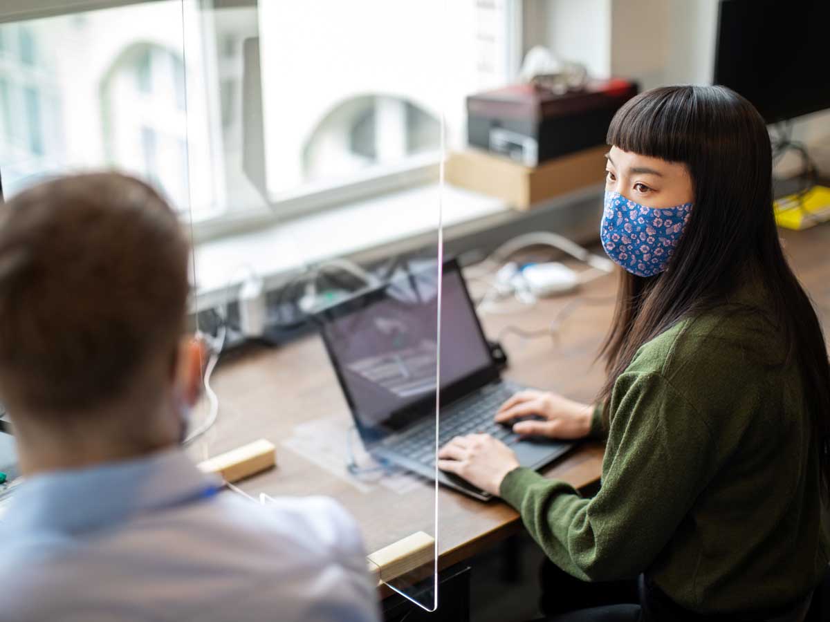 Homme d'affaires et femme d'affaires assis au bureau avec garde de protection entre eux discuter de travail post pandémie Covid-19