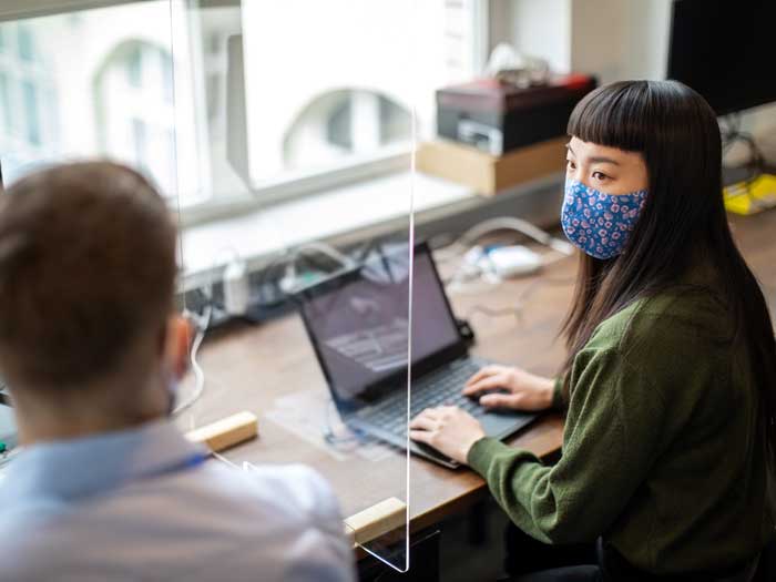 Businessman and businesswoman sitting at desk with protection guard between them discussing work post covid-19 pandemic