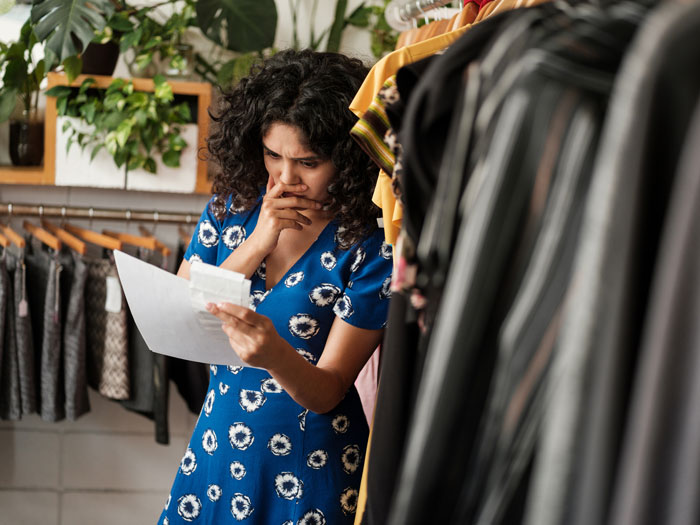 Femme d'affaires inquiète debout dans un magasin de vêtements à la recherche de papiers dans sa main.