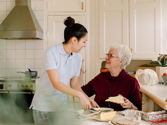 Smiling retired elderly woman talking with female caregiver in kitchen