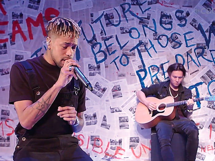 Neon Dreams’ Frank Cadillac performing for a virtual concert inside a room covered in papers and hand-written quotes.