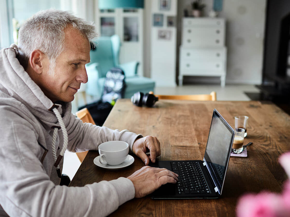 Un homme travaillant sur son ordinateur et buvant du café dans sa cuisine.